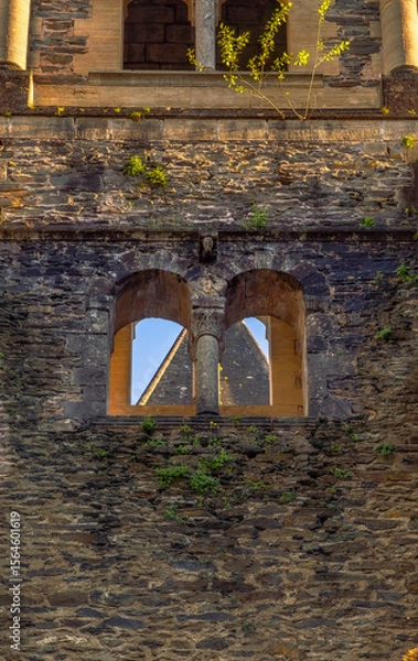 Fototapeta Close-up of a Romanesque stone window with arches and a column, and plant branches on the stone wall illuminated by evening light at the Abbey of Sainte-Foy, Conques.