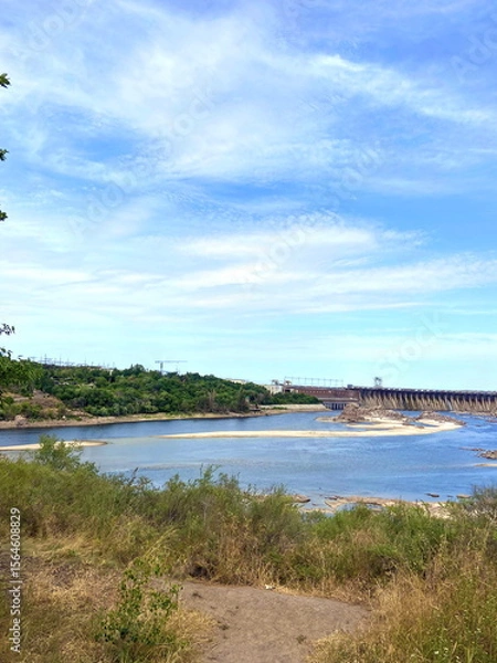 Fototapeta View from the thickets of Khortytsia island on the Dnieper dam under a blue spring sky shaded by a cloud cover.