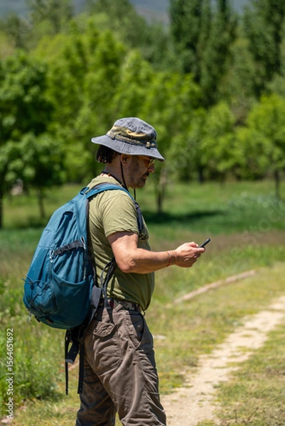 Fototapeta Middle-aged adventurer checking his cell phone on a forest trail