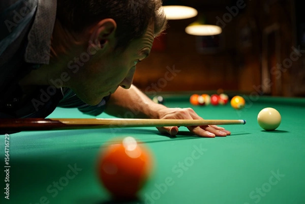 Fototapeta Close-up of a pool player aiming cue at white ball on green table, capturing focus and precision in mid-shot.