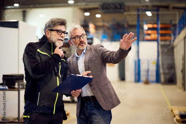 Fototapeta Two Professionals Discussing Work In An Industrial Warehouse Environment