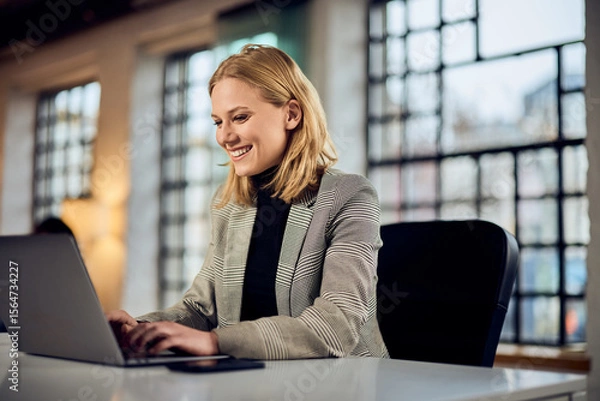 Fototapeta Professional Woman Working on Laptop in Bright and Open Office Setting