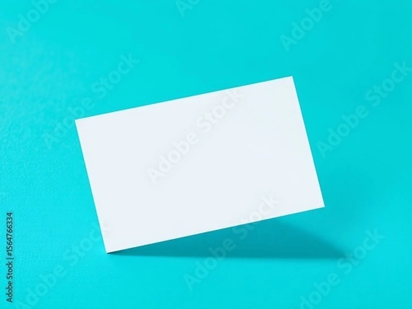 Fototapeta A clean white blank business card floats diagonally on a bright turquoise textured surface creating a minimalist and modern composition