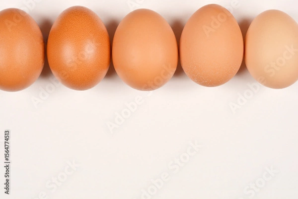 Obraz Five brown eggs are perfectly lined up across the top of a simple, light background, providing ample space below for text or design elements