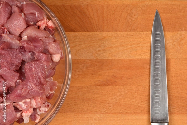 Obraz Diced pork pieces in a glass bowl and a knife blade on a wooden cutting board