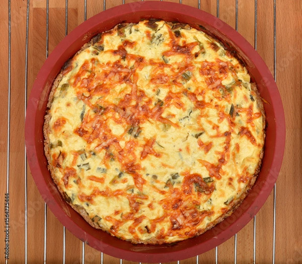 Obraz A top-down shot shows a baked cheese and green onion pie with a golden-brown, slightly crispy top in a red baking dish on a wire rack