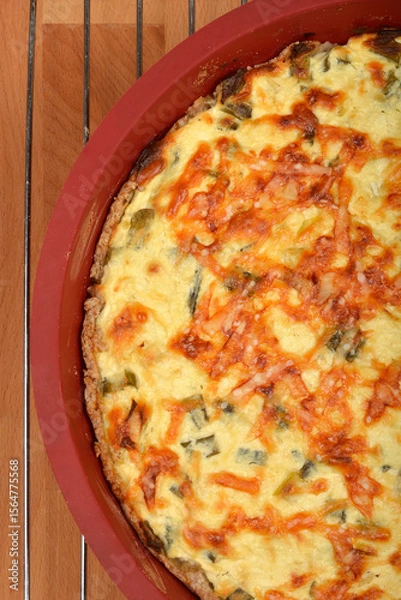 Obraz A top-down shot shows a baked cheese and green onion pie with a golden-brown, slightly crispy top in a red baking dish on a wire rack