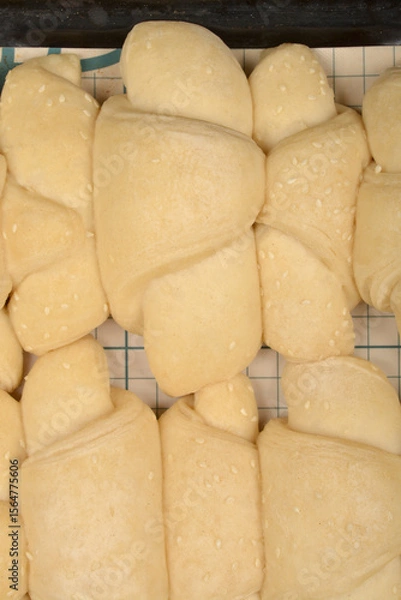 Obraz A close-up overhead shot shows rows of raw, pale yellow mini croissants sprinkled with sesame seeds on a grid surface