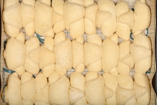 Obraz A close-up overhead shot shows rows of raw, pale yellow mini croissants sprinkled with sesame seeds on a grid surface