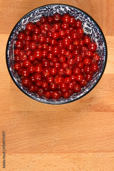 Obraz A top-down shot of a decorative blue and white bowl filled with vibrant red currants, placed on a light wooden surface with ample copy space below