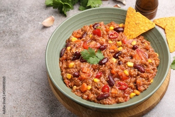 Fototapeta Tasty chili con carne in bowl and nachos on grey table, closeup. Space for text