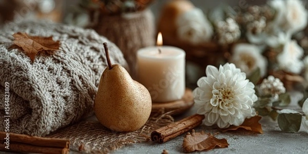 Obraz Cozy autumn-themed still life with bitten pear, candle, white flower, cinnamon, knitted blanket, and fall leaves evoking warmth and seasonal home decor
