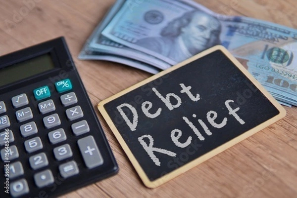 Obraz A blackboard with "Debt Relief" written in chalk, a calculator and US dollar bills. Financial solutions, managing debt concept.