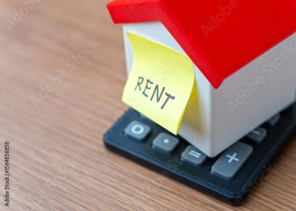 Obraz A miniature house on top of a calculator and a yellow sticky note with the word "RENT". Housing expenses, and property management concept.