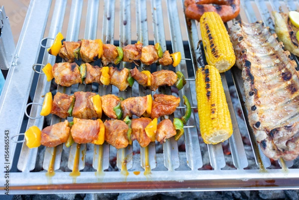 Fototapeta Pork and pepper skewers grilling with corn on the cob and ribs