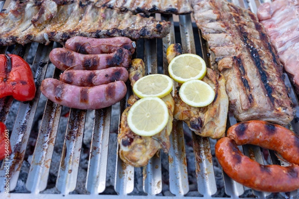 Fototapeta Sausages, chicken with lemon and pork ribs grilling on barbecue