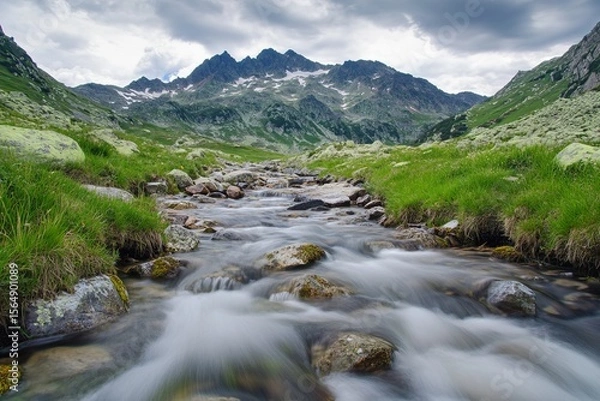 Fototapeta Majestic alpine mountain landscape with clear river stream flowing over rocks and green meadows under blue sky