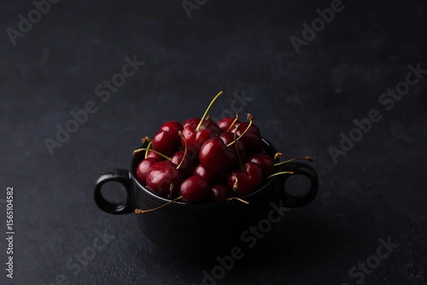 Fototapeta Juicy ripe fresh cherries in a black plate on a black background. Seasonal fruits, harvest. Selective focus, close-up.