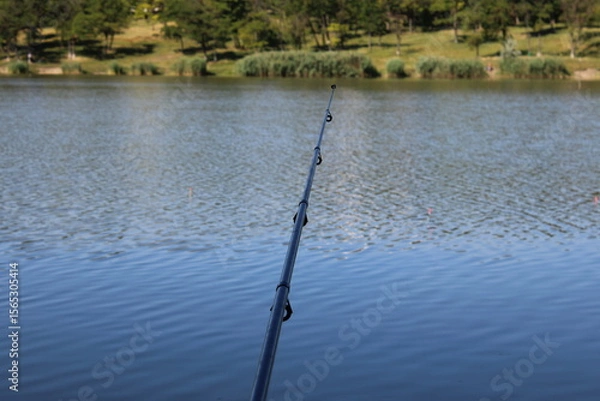 Obraz Fishing rod over a calm lake with trees.
