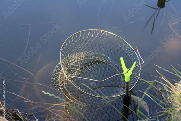 Obraz A fishing net partially submerged in still pond water.