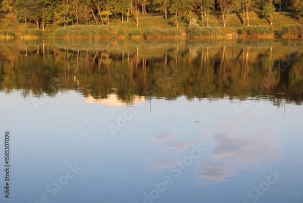 Obraz Calm lake reflecting trees and sky at sunset.