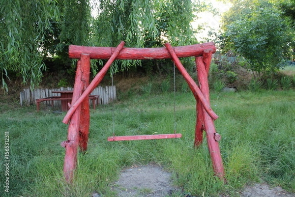 Obraz Red wooden swing set in a verdant garden.
