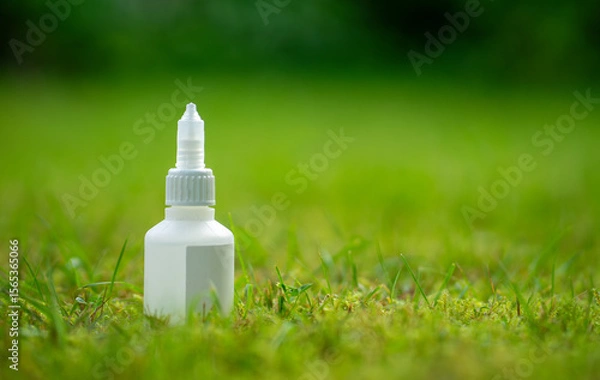 Fototapeta A bottle of cyanoacrylate glue stands on the green grass. Super glue for instant bonding of plastic.