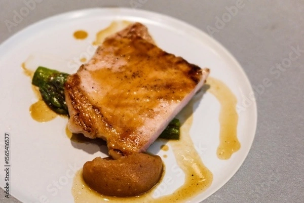 Fototapeta close up of grilled pork loin ( pork chop) with Caramelised Apple sauce resting on a bed of vibrant green asparagus on a white and grey plate
