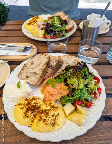 Obraz Close-up of a balanced breakfast meal on a decorative plate.A savory breakfast served at an outdoor cafe, featuring a generous platter with benedict eggs, salmon, fresh salad, and bread.