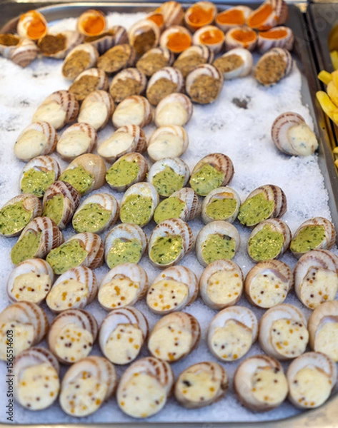 Obraz An assortment of fresh French escargots prepared with various fillings like garlic butter, cheese, and herbs, displayed on ice at a food market. Gourmet street food.