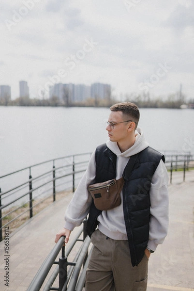 Fototapeta a handsome man of European appearance stands on the embankment in a big city against the background of a river