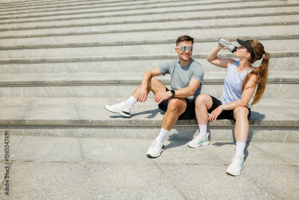 Fototapeta Friends enjoying a refreshing break while exercising on outdoor steps in sunny weather