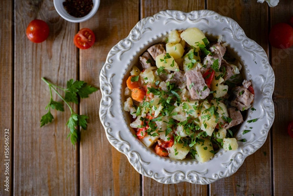 Fototapeta Potatoes with meat on a beautiful white plate on a wooden table. Roast with meat and vegetables for dinner. Close-up