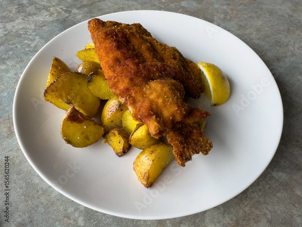 Fototapeta Crispy fried fish with roasted potatoes and lemon on white plate