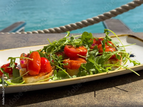 Fototapeta Fresh bruschetta with arugula and cherry tomatoes by the sea