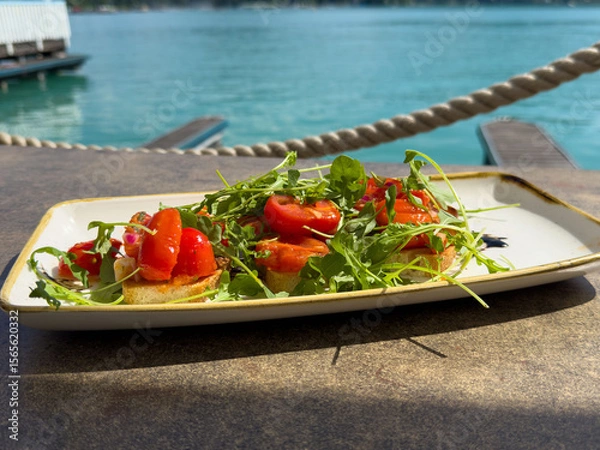 Fototapeta Fresh tomato and arugula bruschetta by lakeside dock on sunny day