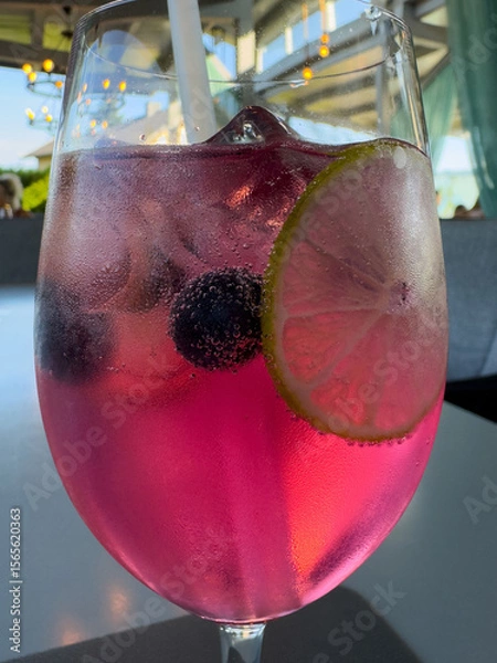 Fototapeta Refreshing pink cocktail with lime and blueberries in a glass with straw