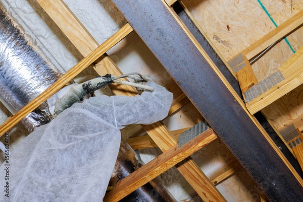 Fototapeta Worker in protective clothing is spray foam insulation at basement as part of home renovation efforts.