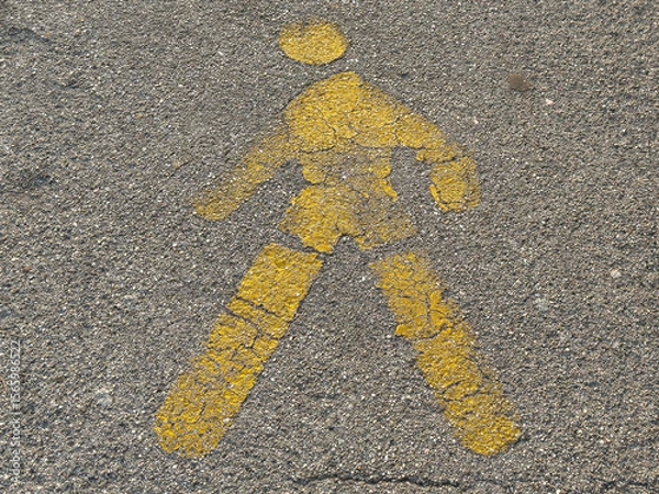 Fototapeta Yellow pedestrian symbol on asphalt: weathered street art for safe walking paths