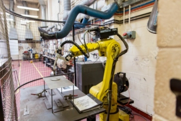 Obraz Yellow industrial robotic arm is clamping metal plate inside safety cage in flat design lab