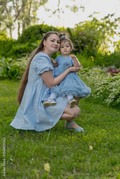 Fototapeta A happy mother and her little daughter in the park. A happy family is resting together on the green grass, and their family life is filled with happiness and harmony