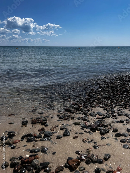 Fototapeta Close-up of wet pebbles scattered on a sandy beach in Odesa, Ukraine, with gentle sea waves sparkling in the background. The sunlit stones create a natural texture and coastal atmosphere, perfect for