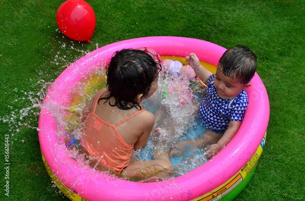 Fototapeta Sisters playing and enjoying in a small swimming pool