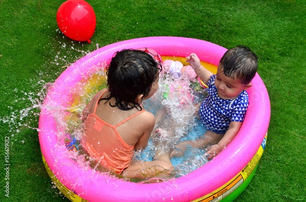 Fototapeta Sisters playing and enjoying in a small swimming pool