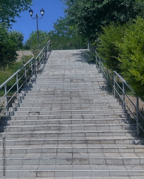 Fototapeta Low angle view of old concrete stairs leading upward towards a metal gate under a blue sky. Symbol of progress, success, and goal achievement.