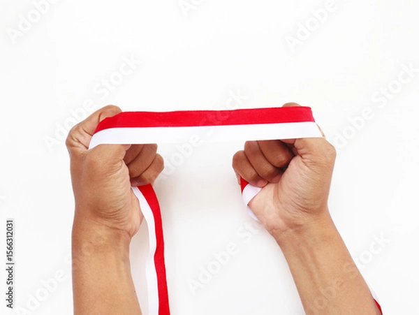 Obraz The hands of a man holding a red and white ribbon as a symbol of the Indonesian flag. Isolated on white background. Independence day concept