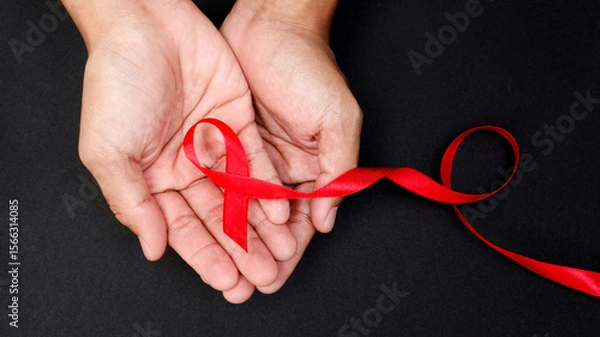 Obraz AID red ribbon in hand on a black background, a symbol of the fight against HIV, AIDS and cancer. concept of helping those in need.