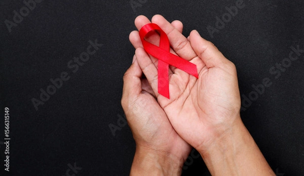Obraz AID red ribbon in hand on a black background, a symbol of the fight against HIV, AIDS and cancer. concept of helping those in need.