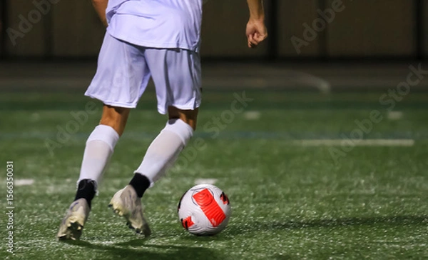 Obraz Soccer Player in White Uniform Dribbling Soccer Ball on Field at Night