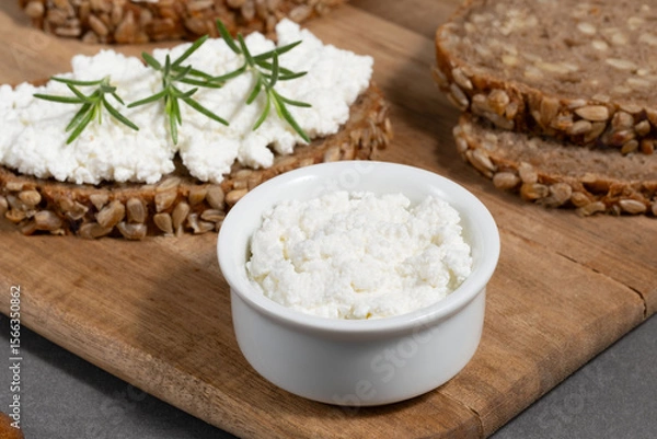 Obraz Delicious rye bread topped with creamy cheese and fresh herbs on a rustic wooden board